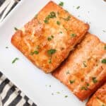 caramelized cooked salmon filets on a white plate with chopped parsley garnish