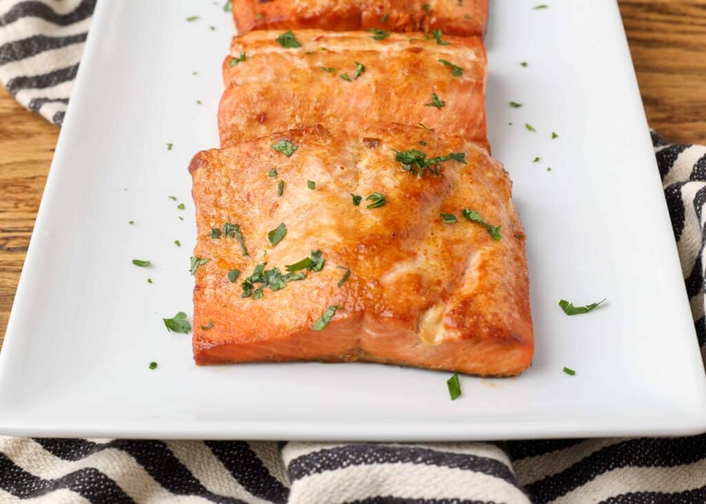 caramelized cooked salmon filets on a white plate with chopped parsley garnish