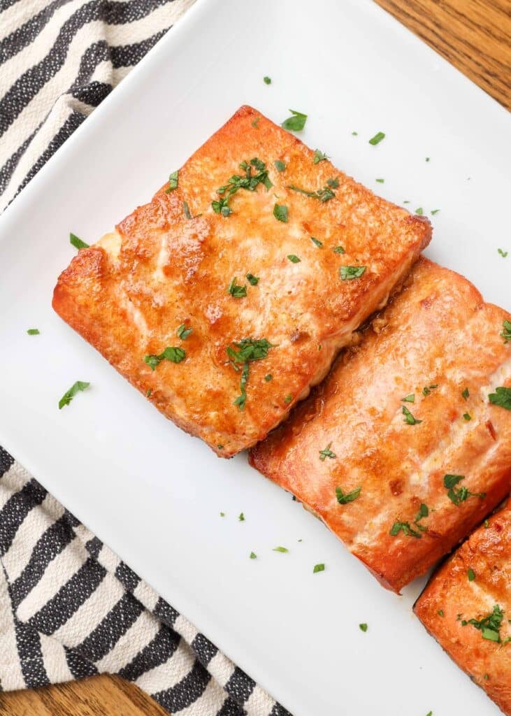 caramelized cooked salmon filets on a white plate with chopped parsley garnish
