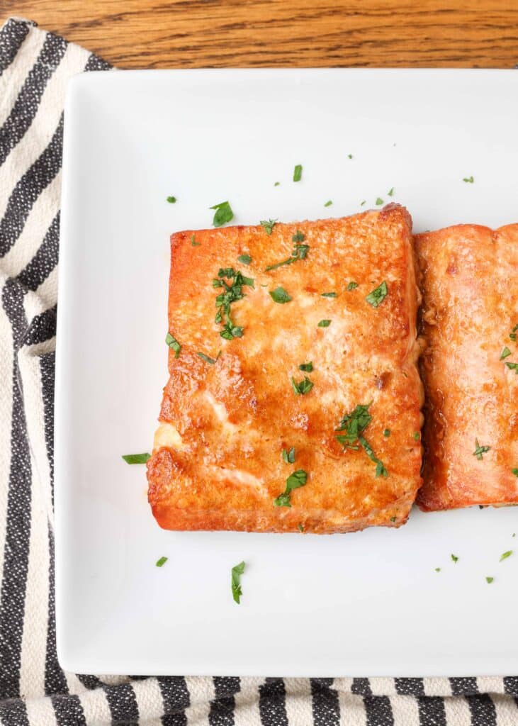 caramelized cooked salmon filets on a white plate with chopped parsley garnish