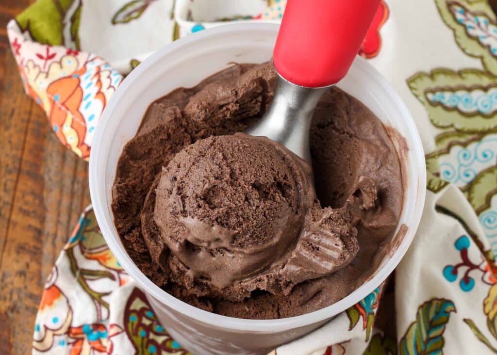 chocolate ice cream with chocolate chips in freezer container with red scoop