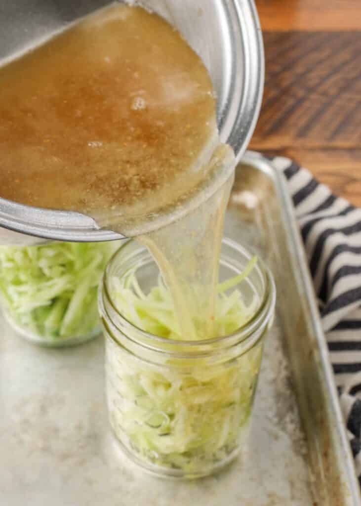 pouring brine over pickled broccoli stems in a jar of brine