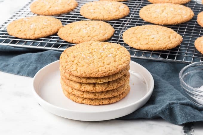 A stack of Cornmeal Cookies on a plate in front of a baking rack filled with cookies.