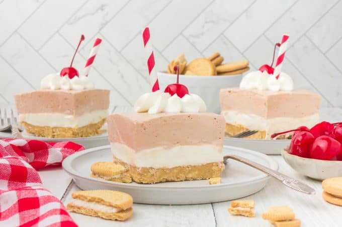 Slices of a lasagna dessert on plates with drinking straws as decoration surrounded by Golden Oreos, cherries and a red and white checkered napkin.