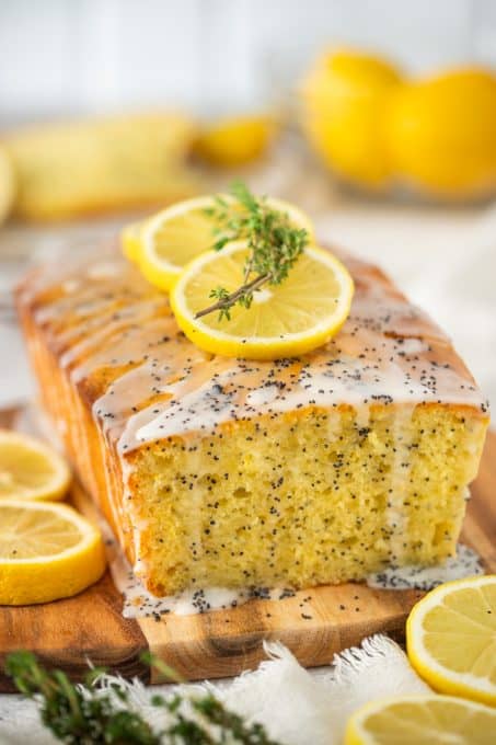 A glazed quick bread on a cutting board decorated with lemon slices.