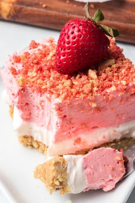 A bite taken out of a no bake dessert made with strawberry gelatin, cheesecake, and cookies.