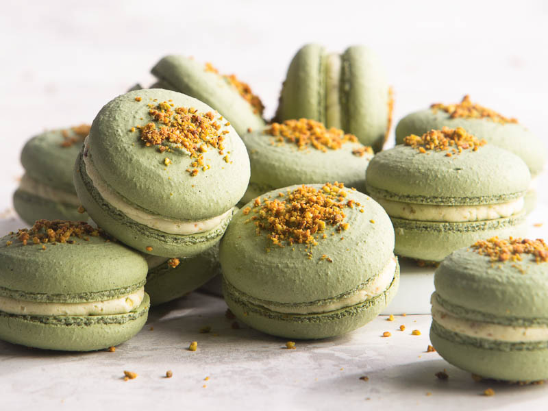 pistachio-raspberry macarons stacked on white surface.