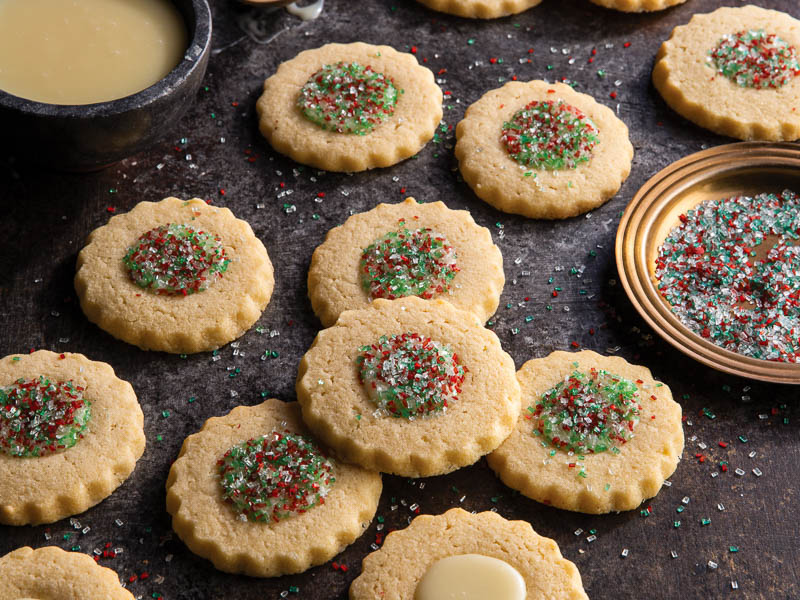 marzipan thumbprint cookies with sparkling sugars on dark surface.