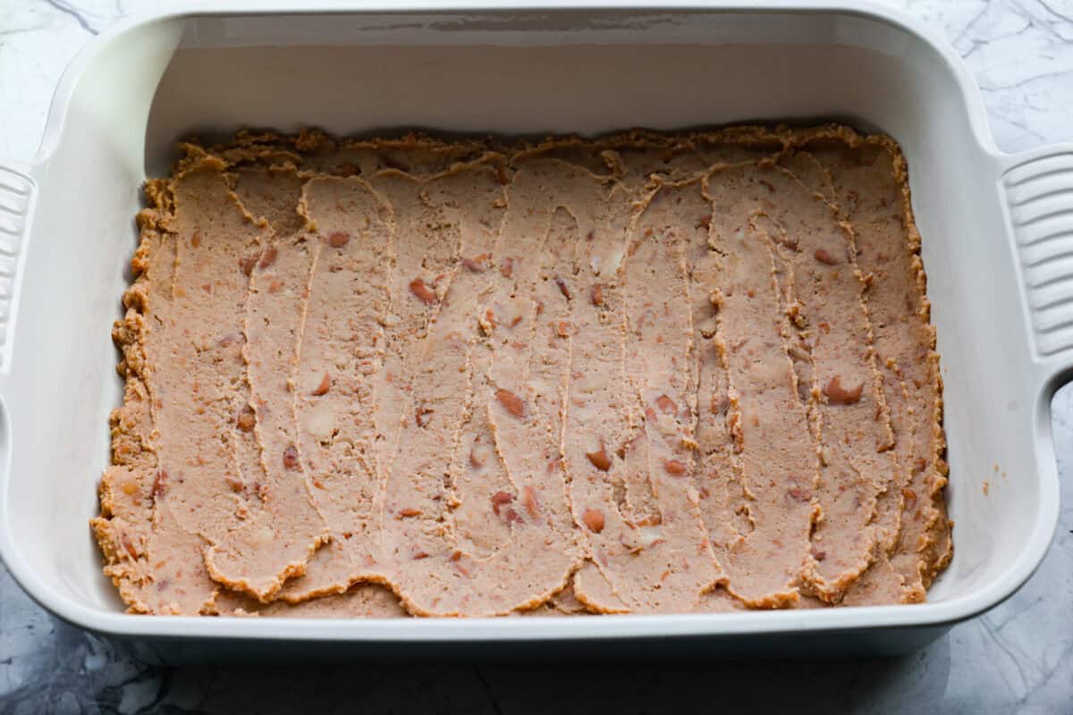 Refried beans spread on the bottom of the baking dish. 
