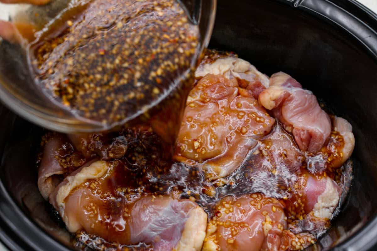 Sauce being poured over the chicken in the slow cooker. 