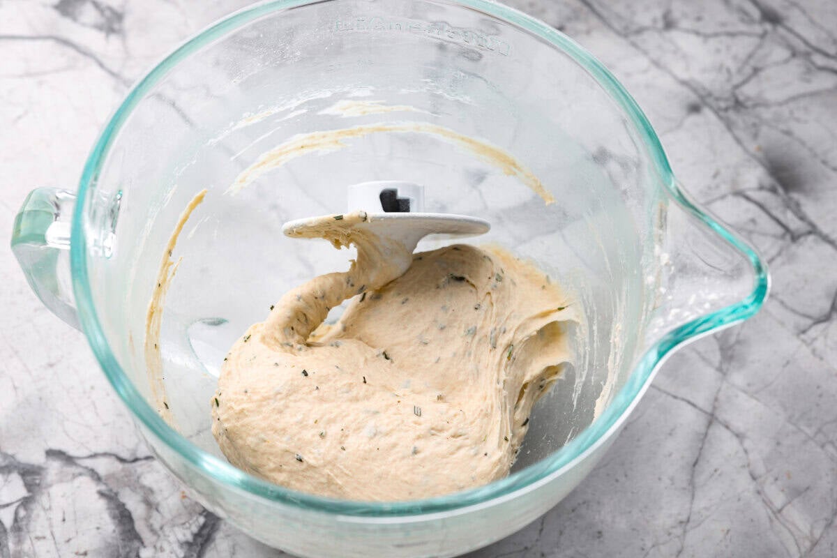 Dough ingredients mixed together with a dough hook in a mixing bowl.