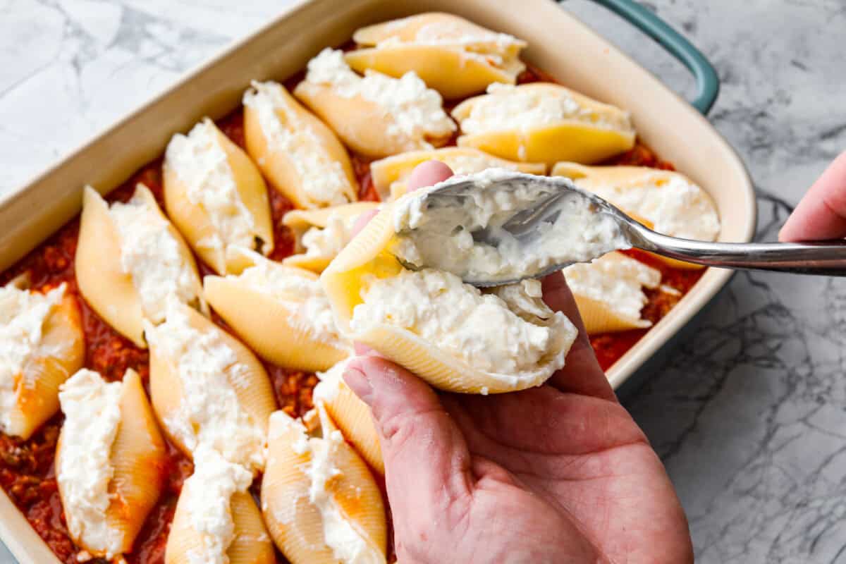 Someone adding a spoonful of million dollar mixture into a jumbo pasta shell. 