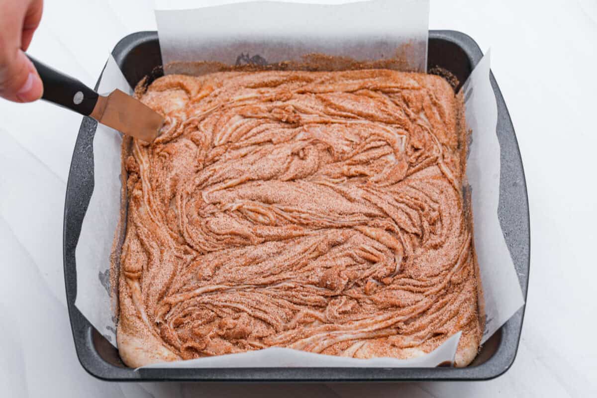 Someone swirling the cinnamon and sugar added to the top of the fudge mixture in the pan. 