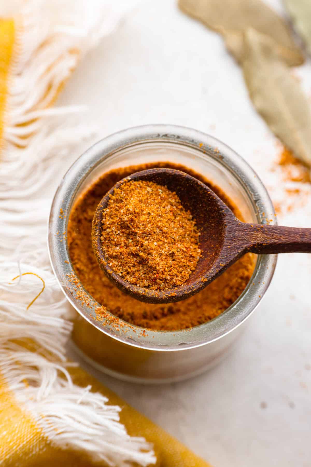 Overhead shot of someone lifting a scoop of seasoning from a jar of homemade old bay seasoning. 