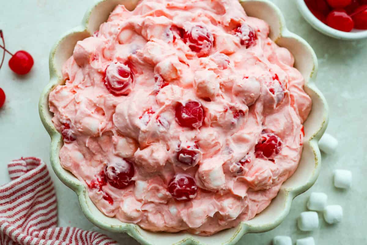 Bowl of cherry cheesecake fluff salad with cherries and marshmallows on the side. 