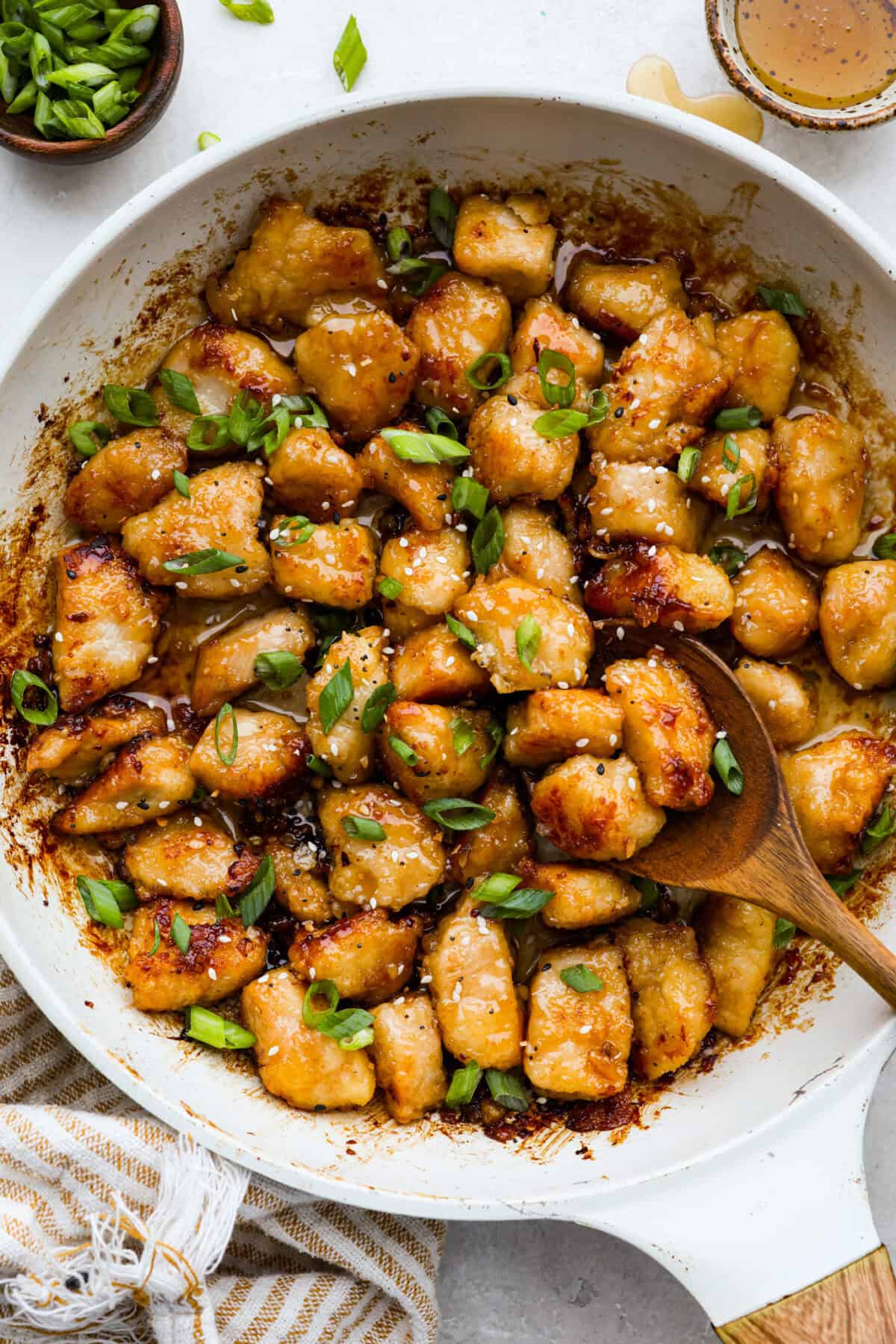 Overhead shot of honey butter chicken in a skillet garnished with sesame seeds and green onions.