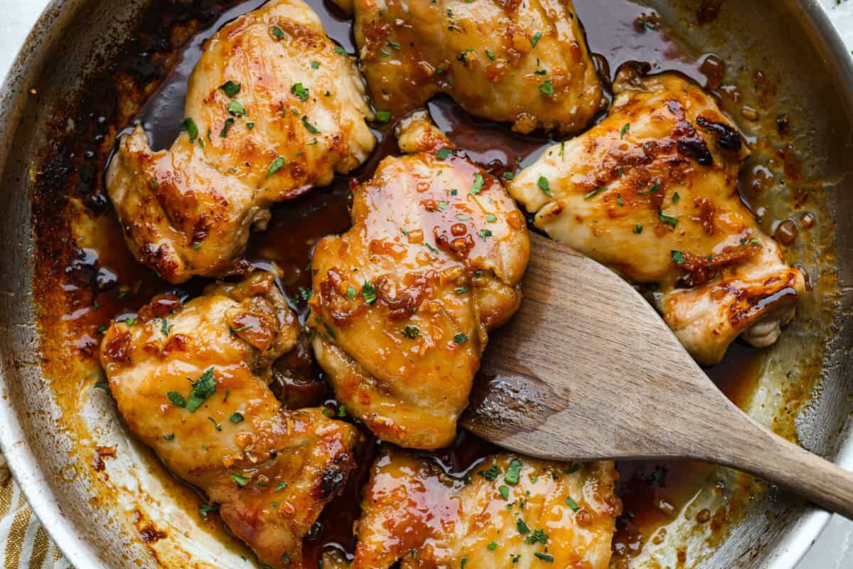 Brown sugar garlic chicken thighs cooking in a pan with a wooden spatula. 