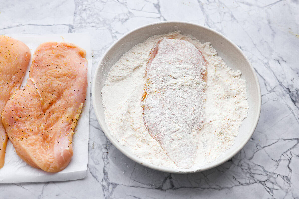 Chicken breast coated in flour in a dish. 