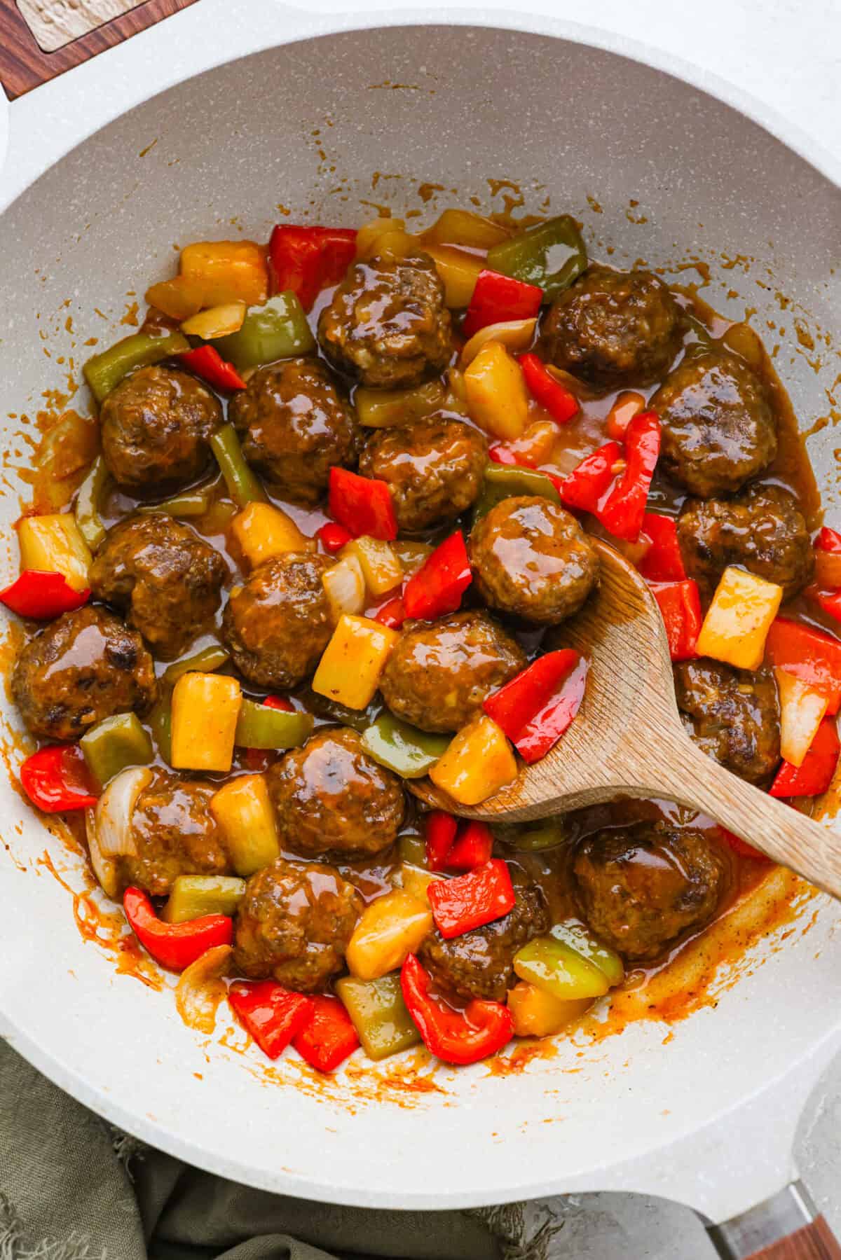 Skillet with sweet and sour meatballs cooking in it with the pineapple and veggies. 