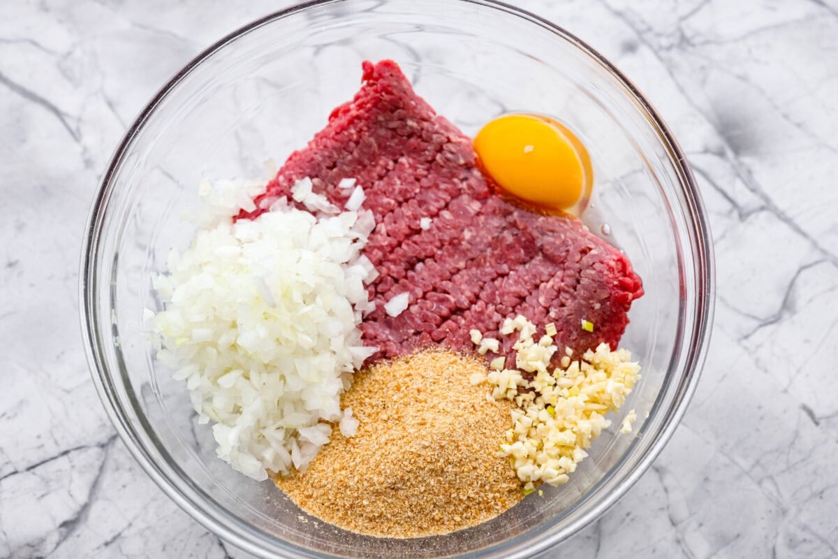Mixing bowl with ground beef, egg, breadcrumbs, onion, and garlic. 