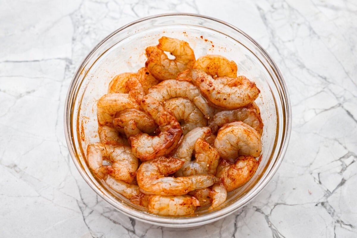 Raw shrimp seasoned in a mixing bowll.