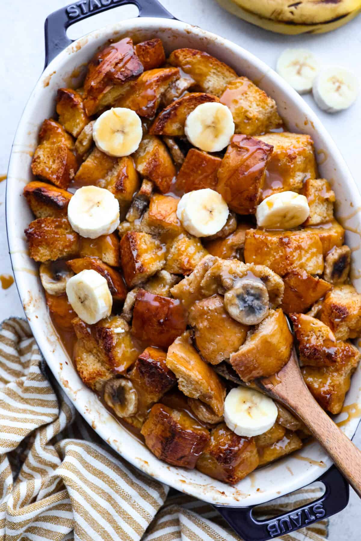 Overhead shot of cooked banana bread pudding drizzled with caramel and topped with sliced fresh bananas. 