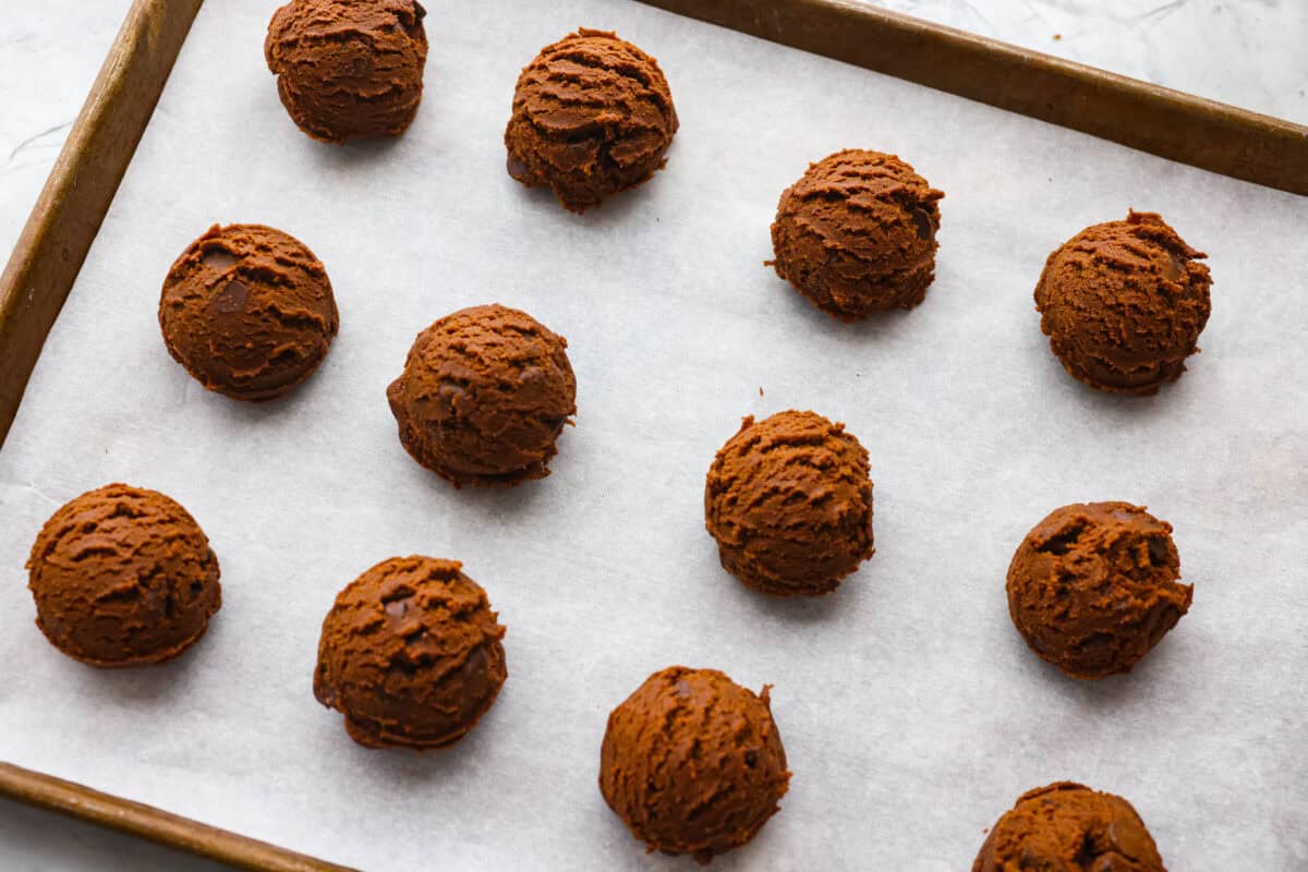 Chocolate peppermint cookie dough balls on parchment paper on a cookie sheet.