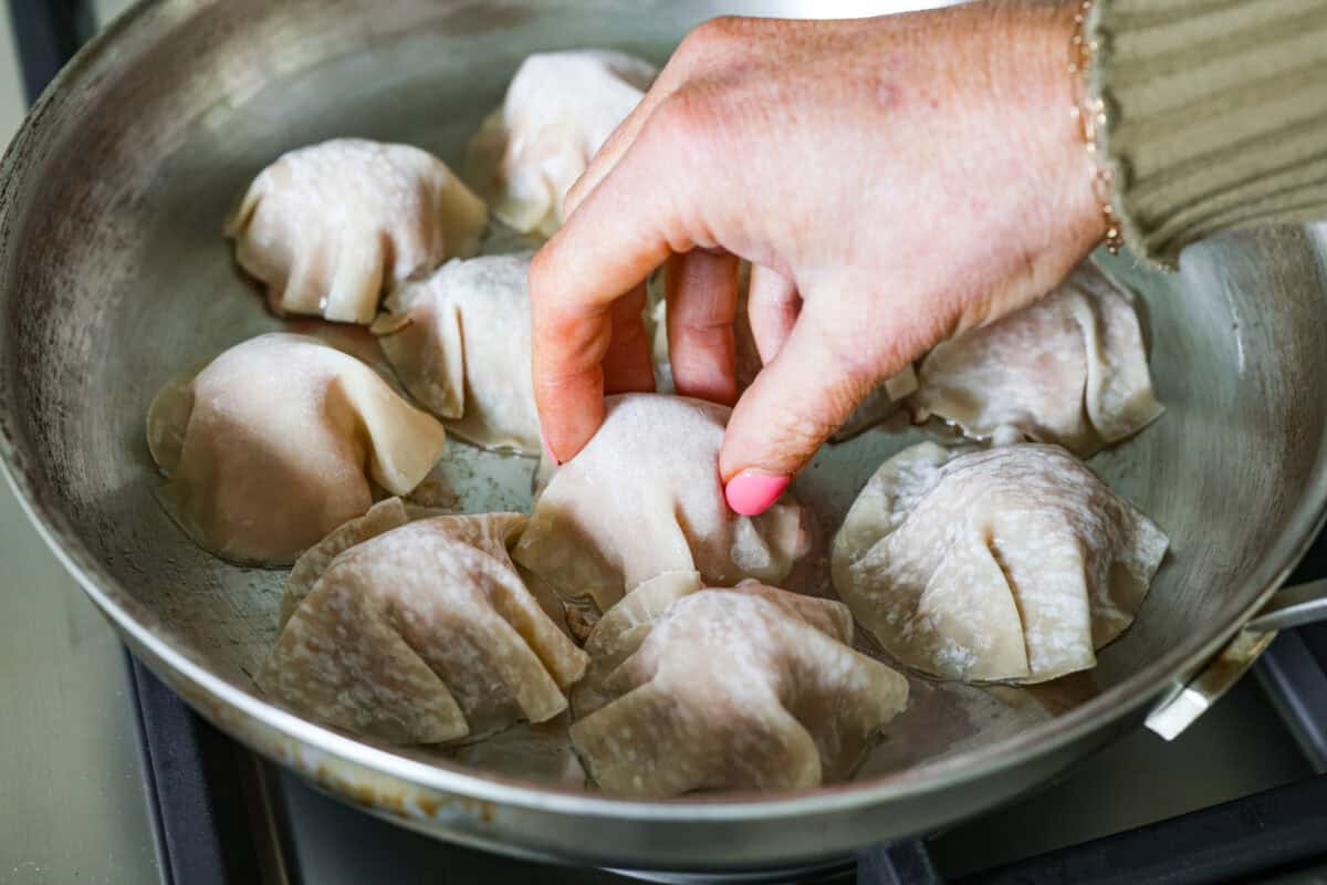 Someone placing wonton wrappers on top of the meatballs in the skillet.