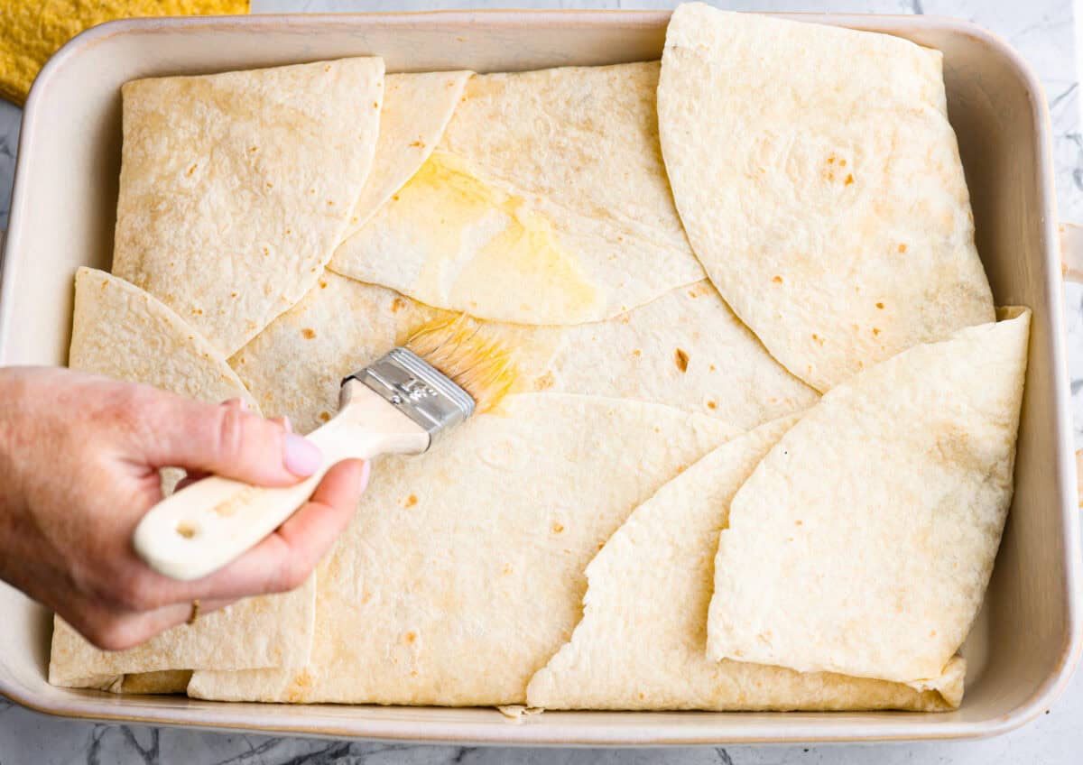 Tortillas folded in over the layers and someone is spreading butter on the the crunchwrap casserole.