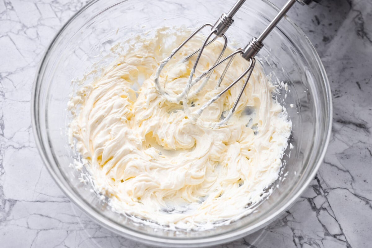 Someone using a had mixer to beat the cream cheese. 