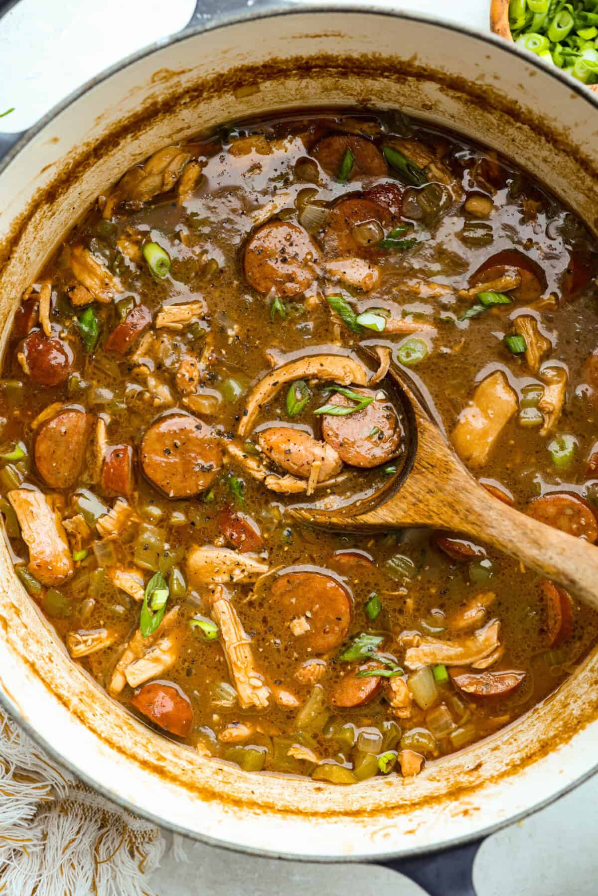 Large pot of chicken and sausage gumbo with a wooden spoon.