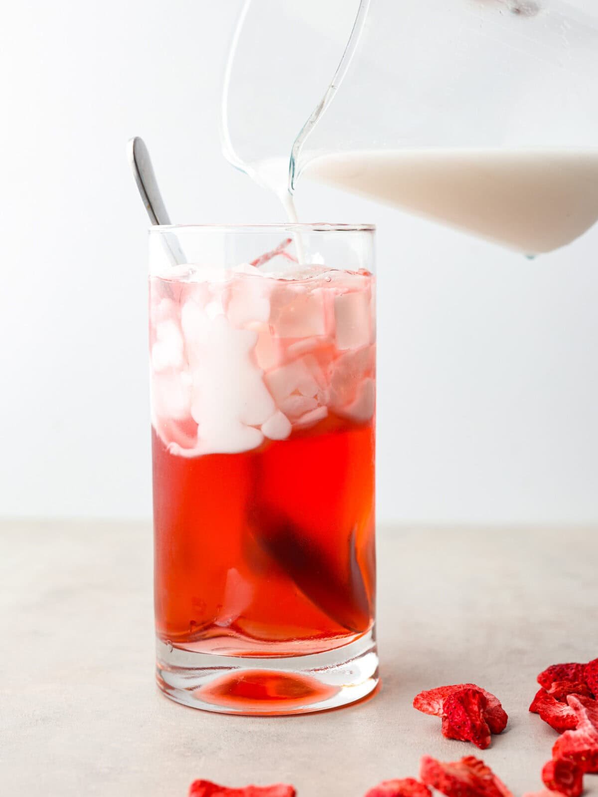 Someone pouring coconut cream into a glass with strawberry acai concentrate. 