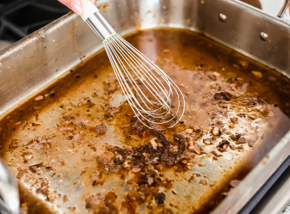 Someone whisking i chicken broth to the roasting pan with pan drippings. 