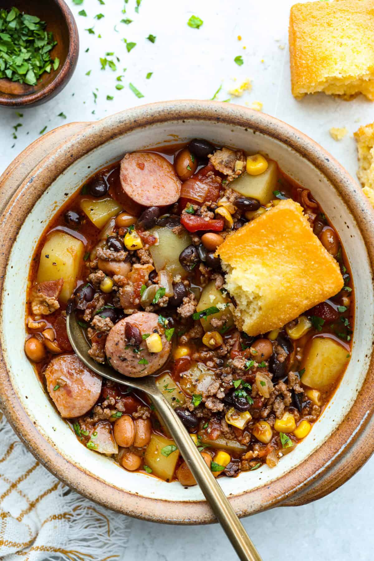 Bowl of Texas cowboy stew with some corn bread and a gold spoon.