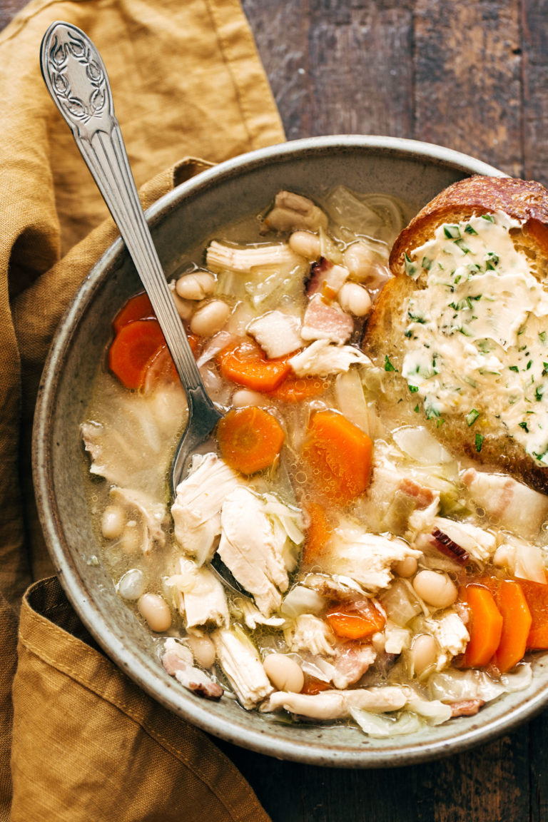 Country chicken stew in a bowl with carrots, beans, and buttered bread.