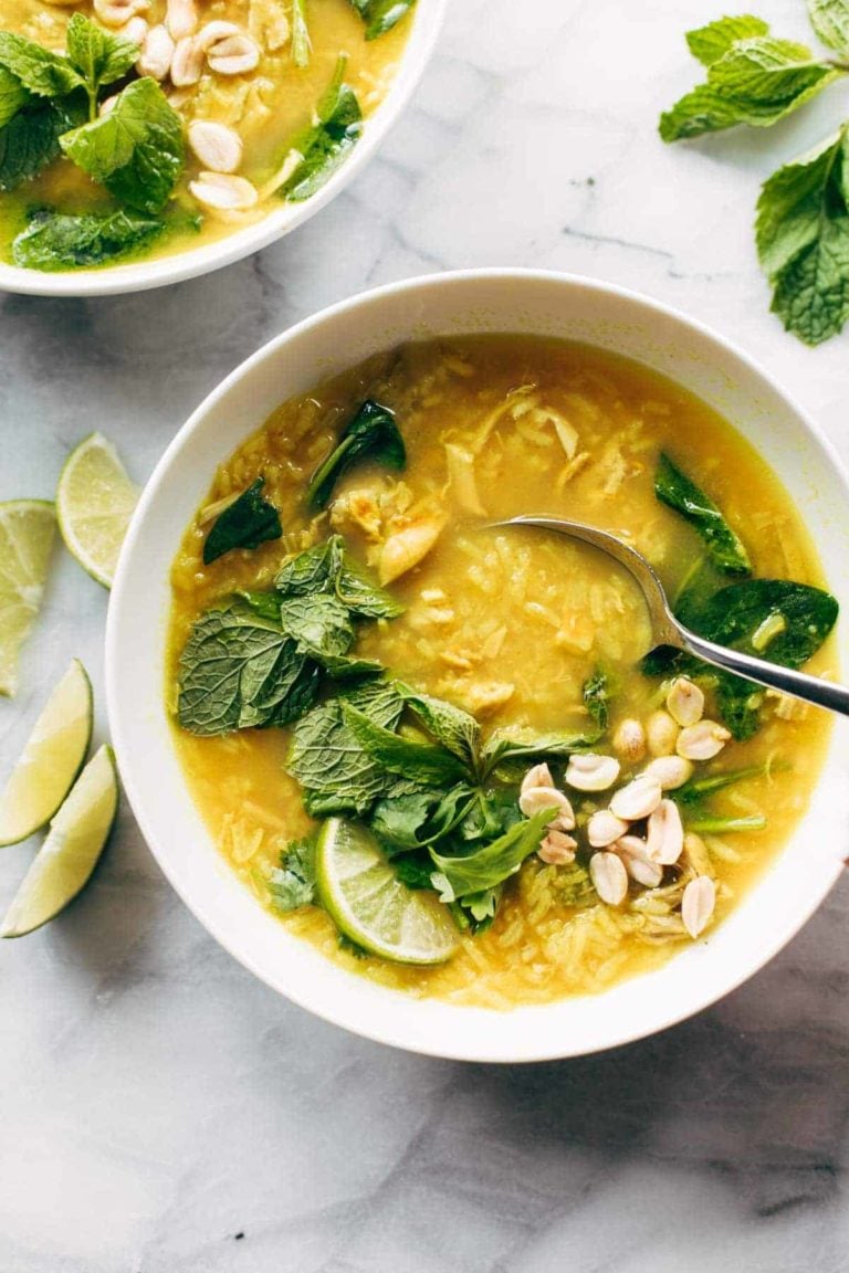 Chicken and rice soup in a bowl with herbs, peanuts, and lime on top.
