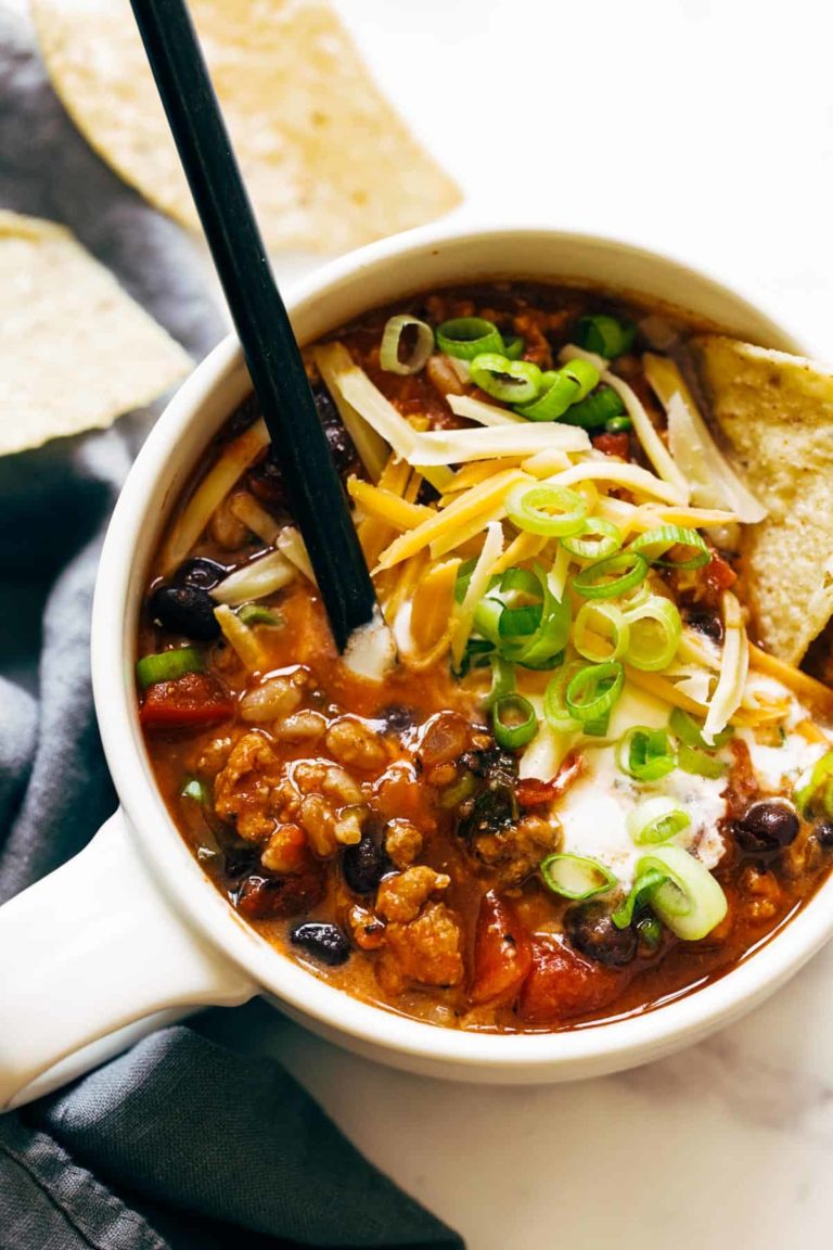 Ancho turkey chili in a bowl with chips, cheese, and green onions on top.