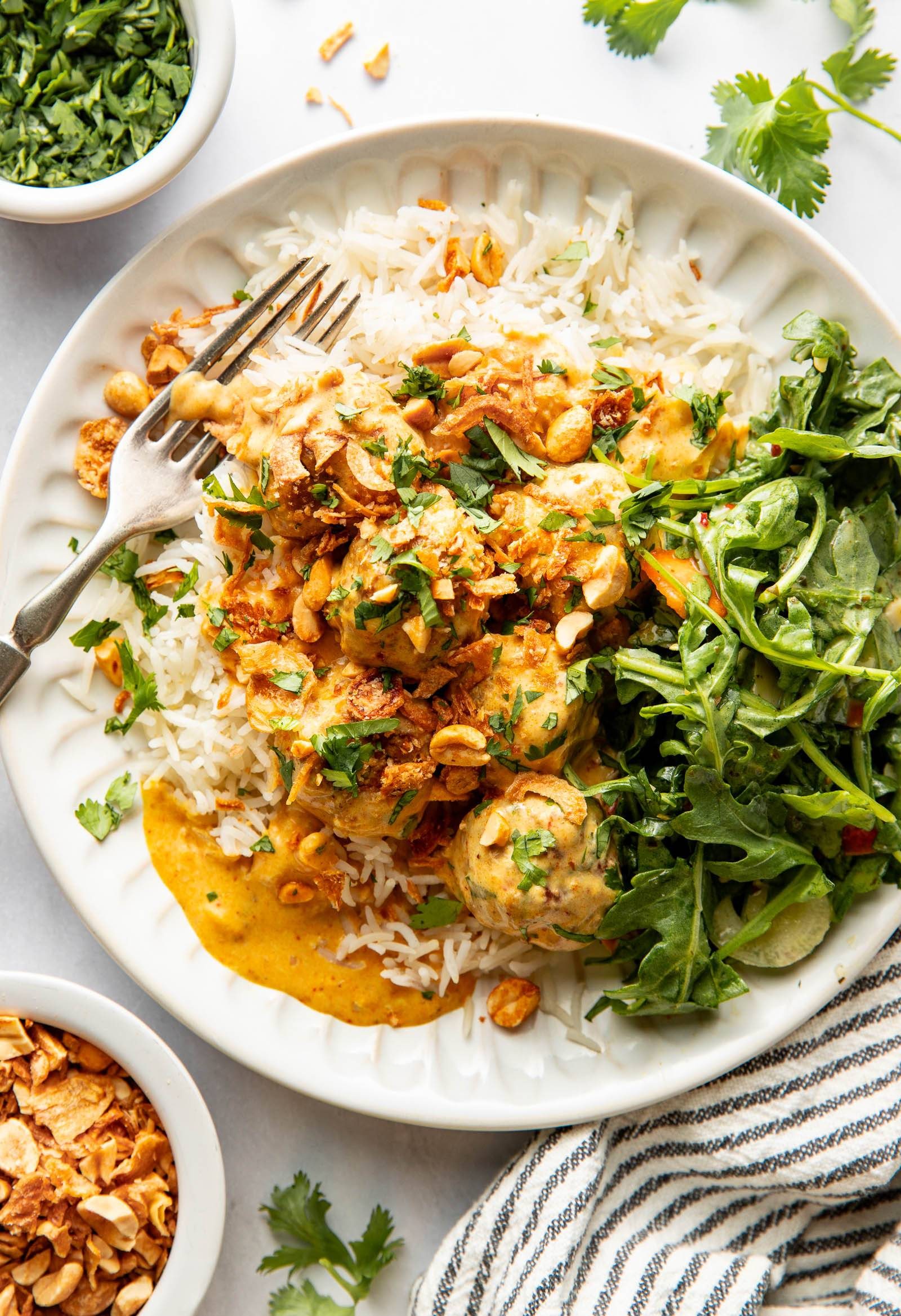 Yellow curry meatballs on a plate with rice and greens.