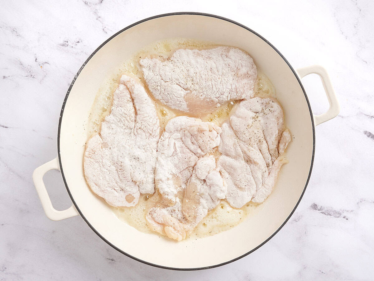 Flour coated chicken breast in a skillet.