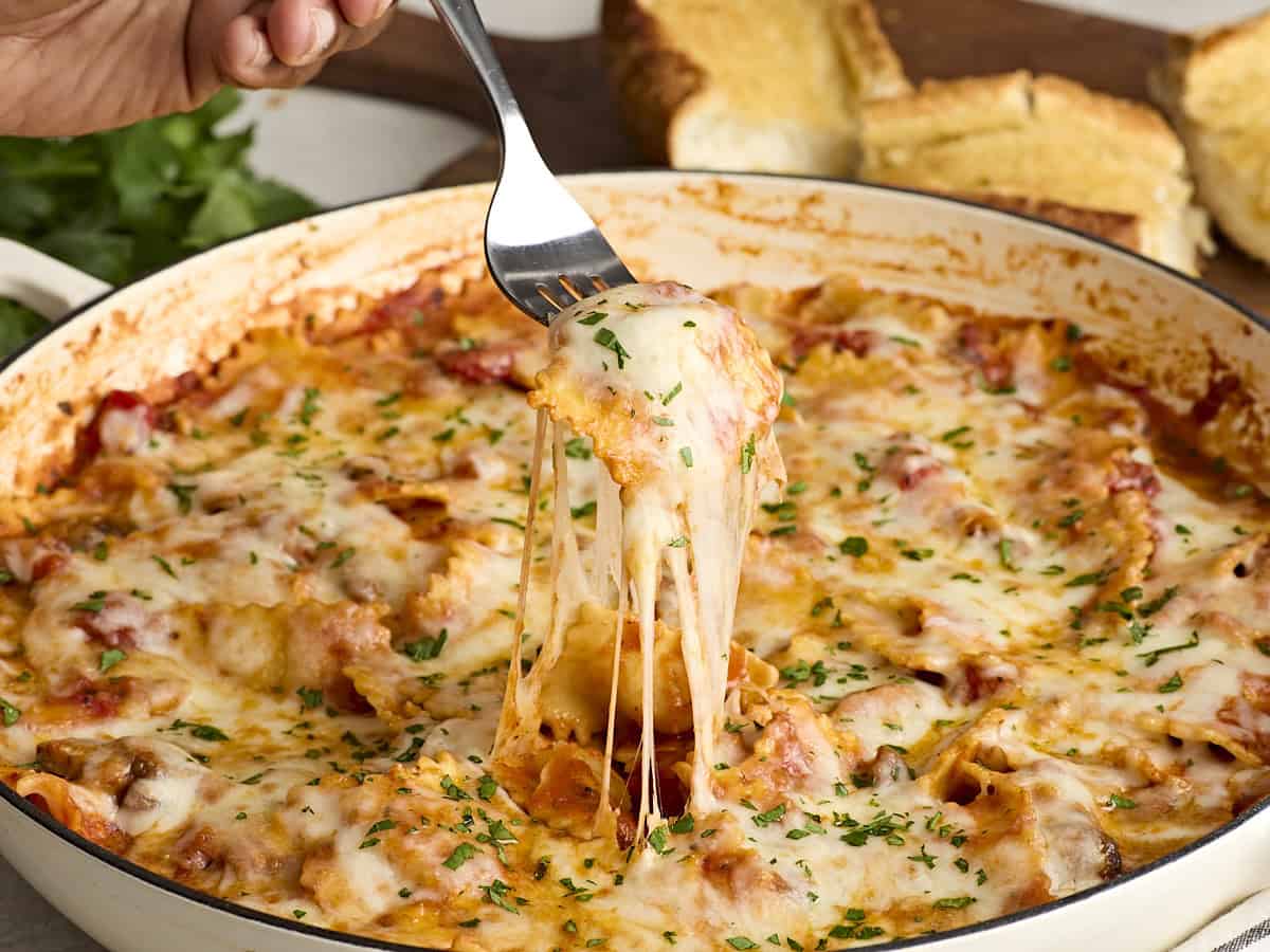 A fork taking some cheesy ravioli from a skillet.