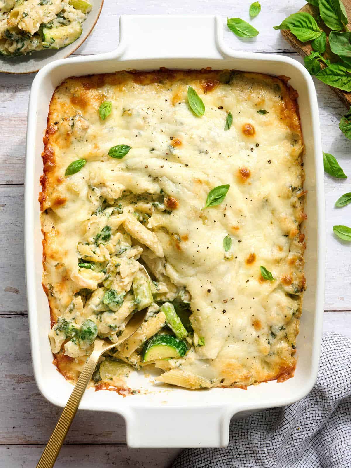 Overhead view of a casserole dish of baked pasta with spring veggies and a spoon.