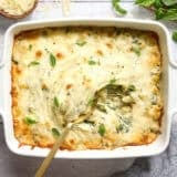 Overhead view of a casserole dish of baked pasta with spring veggies and a spoon.