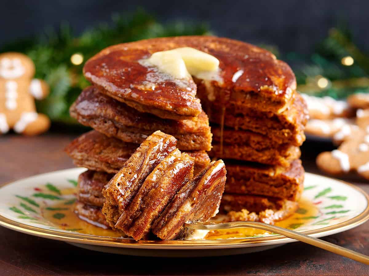 Side view of a stack of gingerbread pancakes with butter and a portion cut away on a fork.