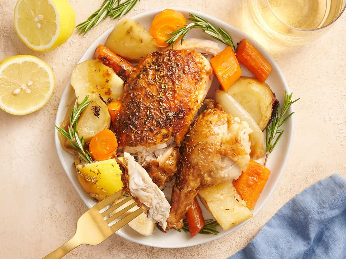 Roast chicken on a plate with vegetables, with a fork taking some.