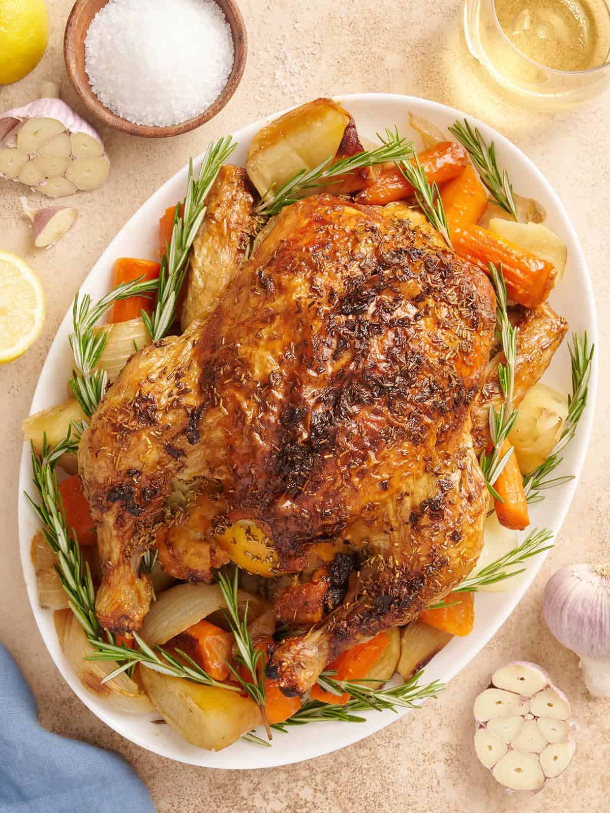 A whole oven roasted chicken on a platter with vegetables.