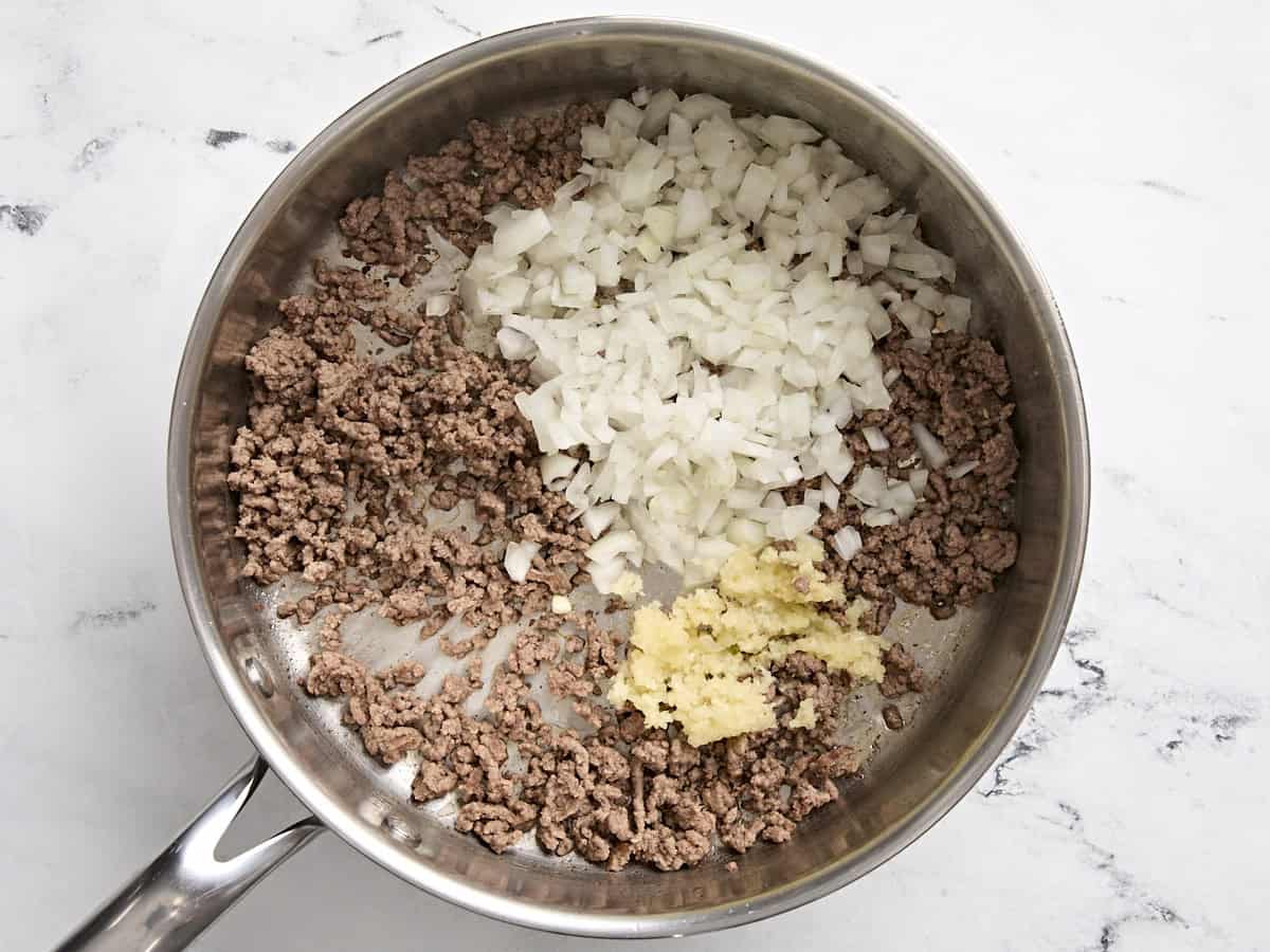 Diced onion and minced garlic added to ground beef in a skillet.