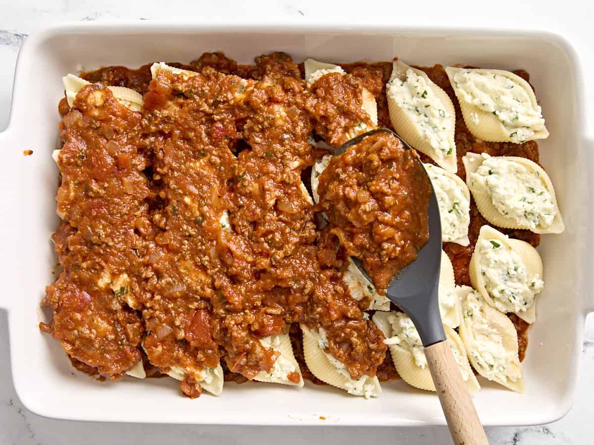 Meat and sauce being added on top of stuffed shells.