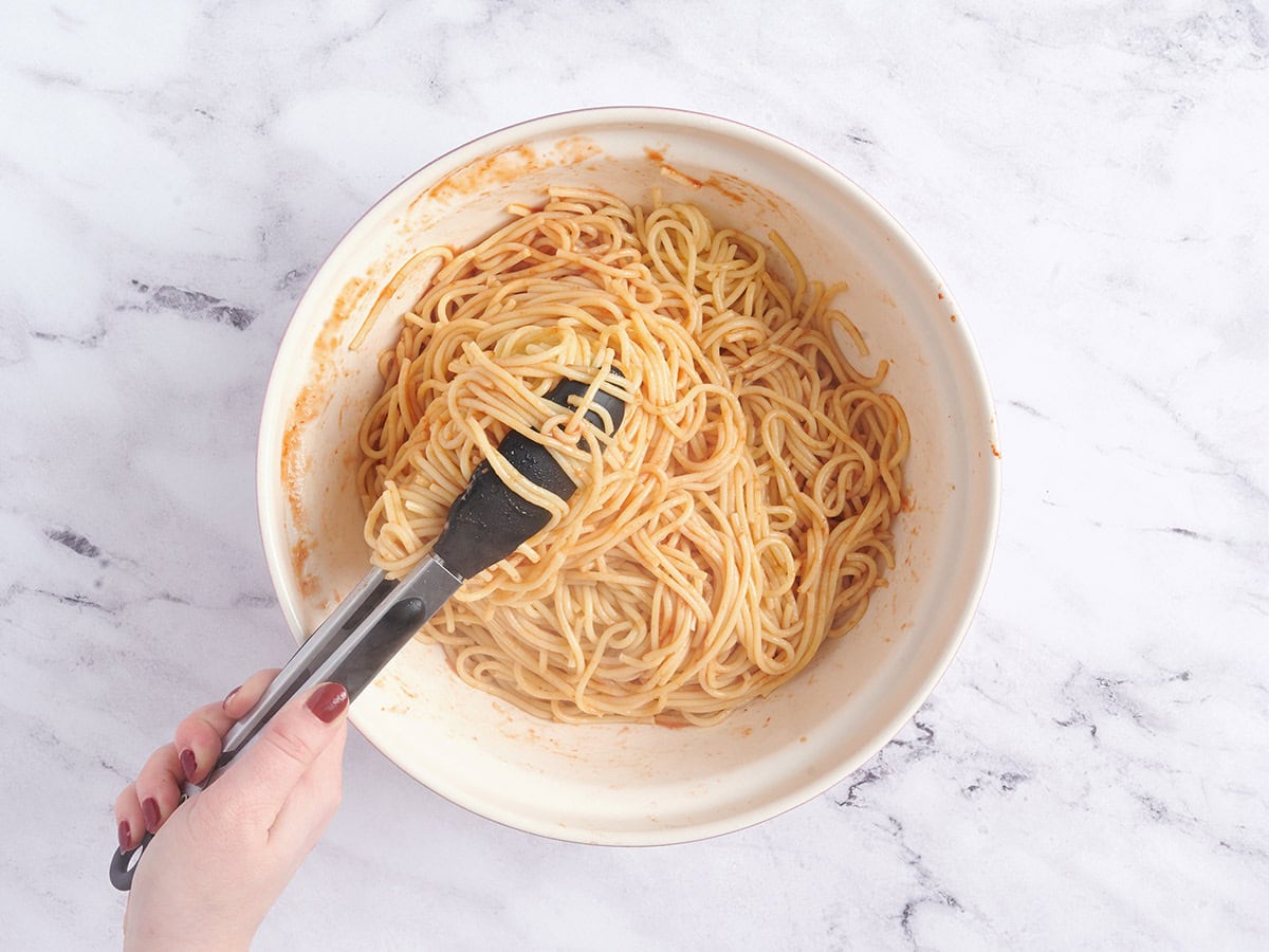 Spaghetti being tossed in water and tomato paste.
