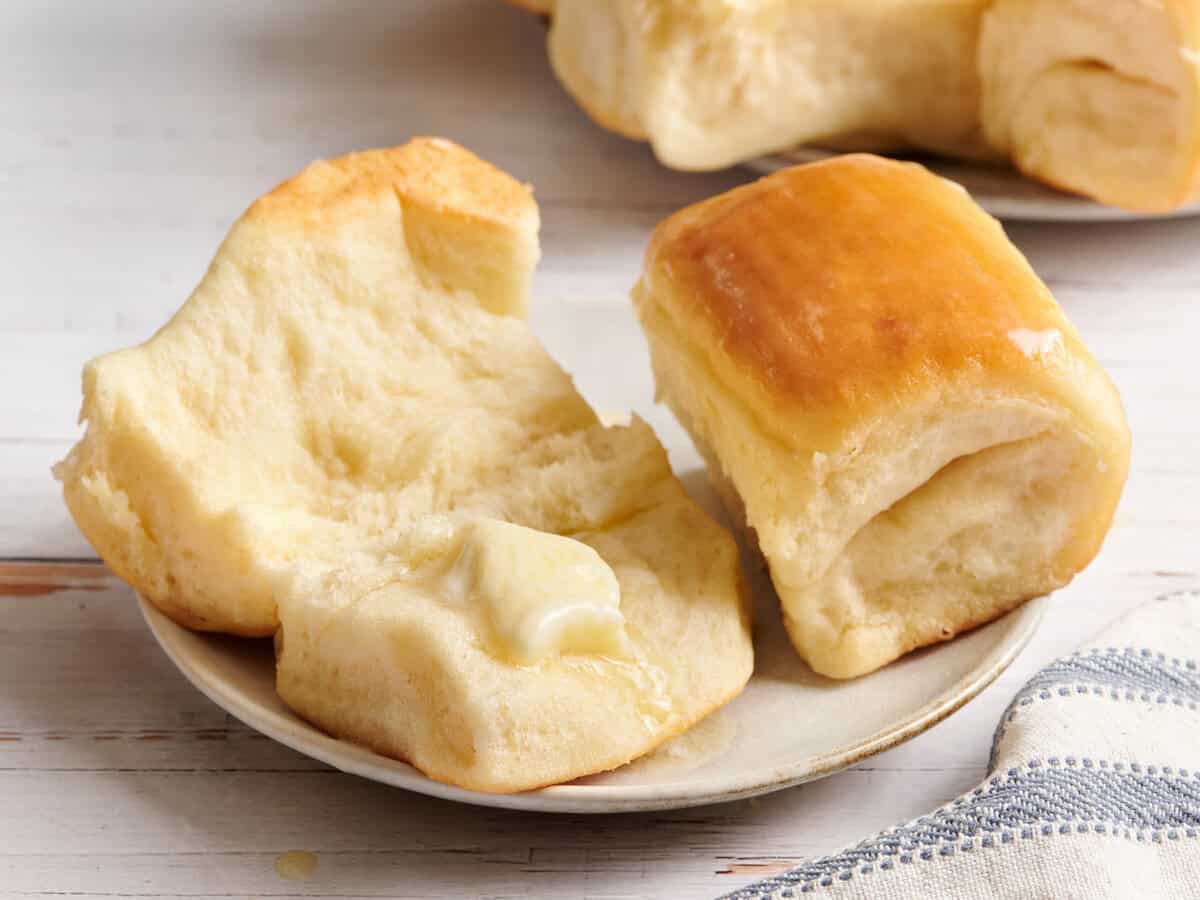 Parker Roll cut in half with a pat of butter on a white plate.