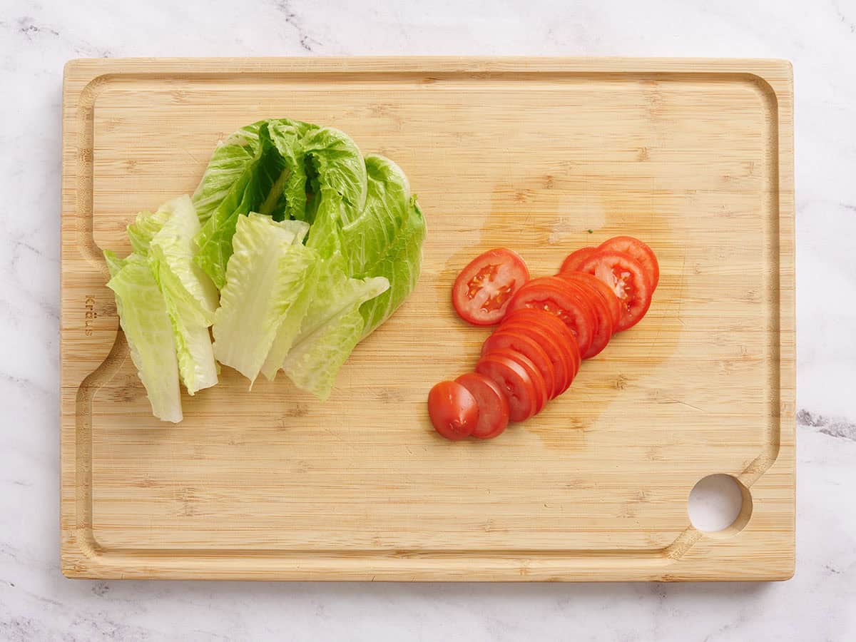 Sliced lettuce and tomatoes on a wooden cutting board.